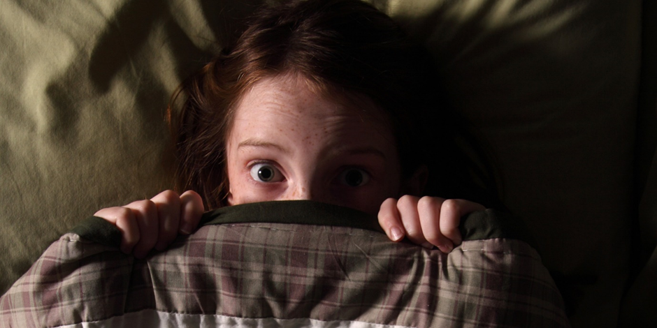 A young girl suffering from nyctophobia pulls her duvet up under her chin.